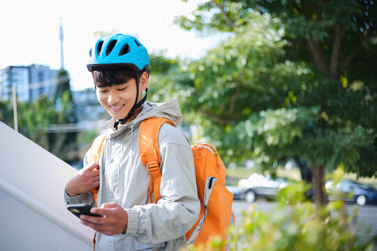 Young Asian delivery guy looking on his phone outdoors.