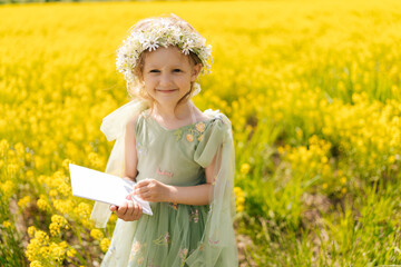 Portrait of cute child girl wearing green fairy dress drawing paint in blank white canvas in...