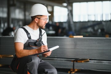 Portrait of a young worker in a hard hat at a large metalworking factory. Shiftman on the warehouse...
