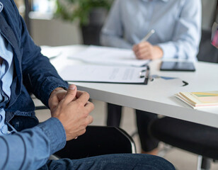 Professional HR photography of job interview with disabled candidate, natural office lighting, authentic professional conversation, accessible interview setup visible, interviewer and candidate's hand