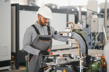 Operator of machine. Industrial worker indoors in factory. Young technician in white hard hat