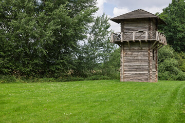 A reconstructed Roman watchtower stands tall in a lush green field, surrounded by dense trees under a bright sky, evoking ancient history in Utrecht