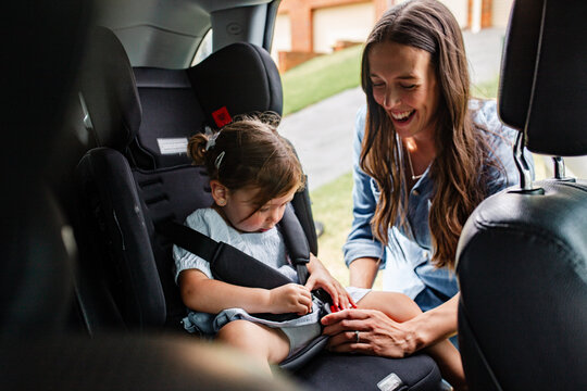Mother fastening seatbelt on toddler daughters car seat.
