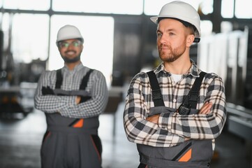 Two male international workers in overalls work together at a machine for the production of...
