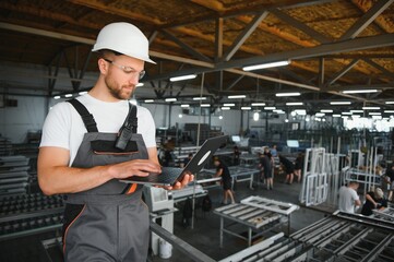 A young male engineer inspects the production of plastic window frames