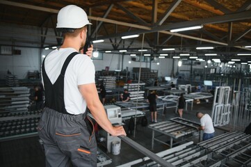 A young male engineer inspects the production of plastic window frames