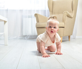 Cute baby girl crawling on the floor in a bright room. Home interior.