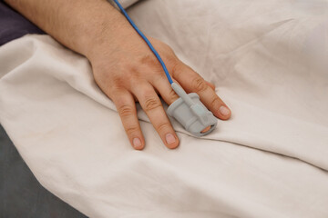 Patient Monitoring Pulse Oximeter Attached to Hand in Hospital Bed. Gray Sensor, Blue Cable, White...