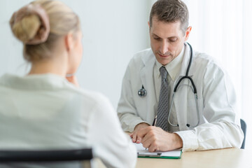 Senior male doctor and female patient discussing in detailed about health concerns and possible treatment plans at hospital. Medicine and health care concept