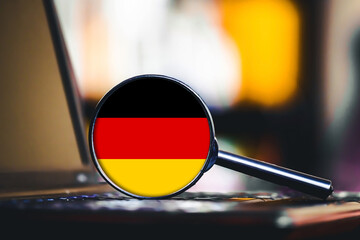 German flag under magnifying glass. Germany symbol on laptop. Search for information. German language or market research. Country analysis. National identity. Digital concept on desk.