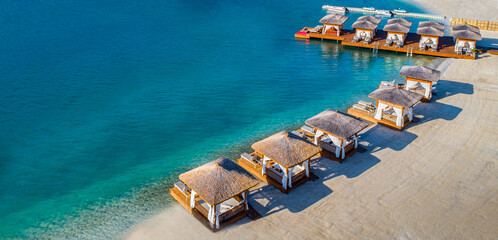 In the touristic holiday resort of Bodrum, there is a crystal clear, turquoise sea and private beach pavilions (bungalows and cabanas) lined up on a luxurious beach. Aerial photo