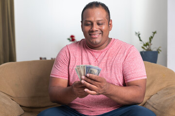 A man in a red shirt is sitting on a couch holding a stack of money