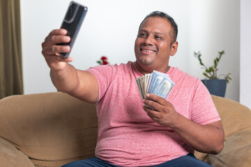 A man is sitting on a couch and taking a selfie with his cell phone