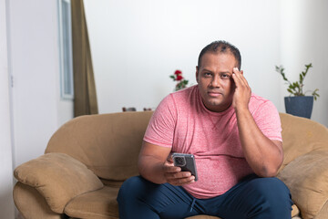 A man in a red shirt is sitting on a couch holding a remote control