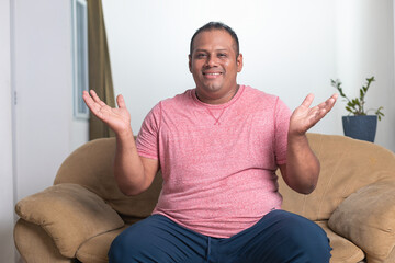 A man in a red shirt is sitting on a couch and making a gesture with his hands