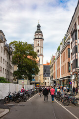 Leipzig, Germany – June 7, 2025:  St. Thomas Church (Thomaskirche) tower rising above a busy street filled with pedestrians and bicycles. church is associated with composer Johann Sebastian Bach.