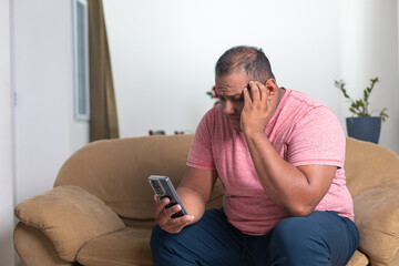 A man is sitting on a couch and looking at his cell phone