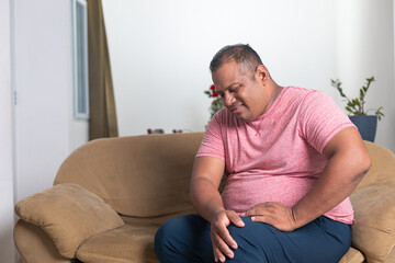 A man in a red shirt sits on a couch with his leg propped up
