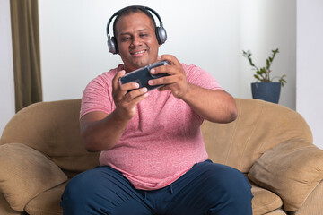 A man in a red shirt is sitting on a couch and playing a video game on his phone