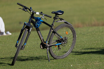 A black mountain bike with blue accents stands on a green grassy field.