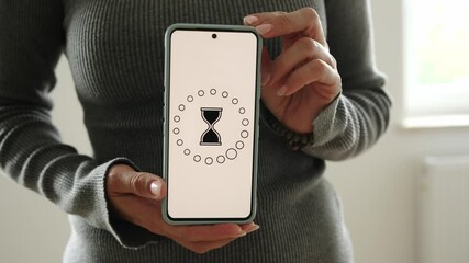Girl Shows A Smartphone With A Loading Process And A Rotating Sandglass Icon On A White Screen - Powered by Adobe
