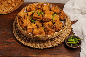 Top angle of golden Tahu Sumedang arranged neatly with fresh green chilies on bamboo plate.