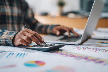 Young adult calculating monthly savings on a laptop with charts and financial statements in view, copy space for finance or economy-themed content.