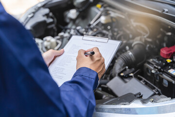 Auto check up and car service shop concept. Mechanic writing job checklist to clipboard to estimate...