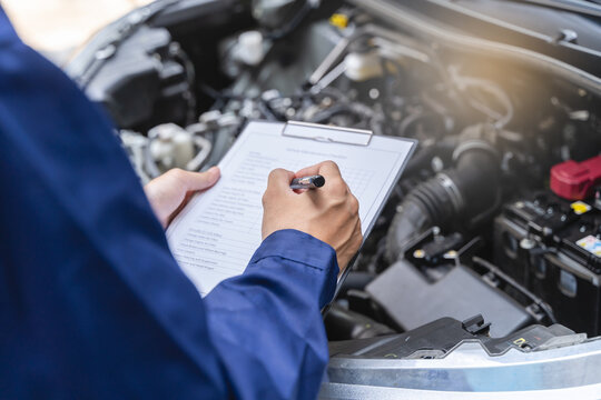 Auto check up and car service shop concept. Mechanic writing job checklist to clipboard to estimate repair quotation to client at workshop garage.