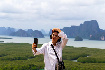 Young woman taking selfie with smartphone on scenic viewpoint overlooking lush green mangroves and...