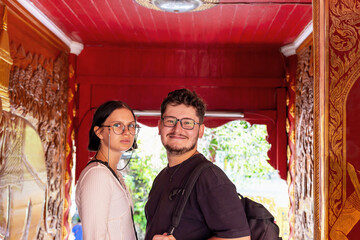 Young couple standing together in vibrant temple corridor surrounded by intricate wall carvings and...