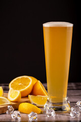Chilled wheat beer with light foam with sliced lemon and ice cubes on rustic wood background. Concept of citrus refreshment, summer beer and craft beverage. Chilled wheat beer with lemon and ice