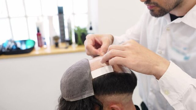 Slow motion, close up view of a hair clinic technician meticulously applying a hair system patch to a client's scalp, demonstrating the detailed process of hair replacement