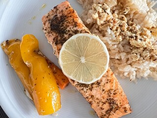 Grilled salmon fillet with herbs and lemon slice served with basmati rice and colorful vegetables, e.g. carrots and yellow bell peppers.