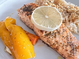 Grilled salmon fillet with herbs and lemon slice served with basmati rice and colorful vegetables, e.g. carrots and yellow bell peppers.