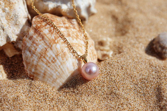 Elegant pearl necklace resting on sandy beach near seashell under bright sunlight