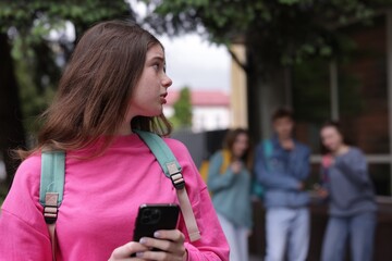 Teenage girl with smartphone suffering from bullying at school, selective focus