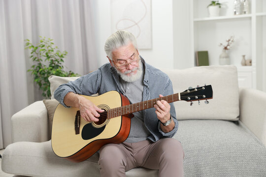 Relaxing hobby. Senior man playing guitar on sofa at home