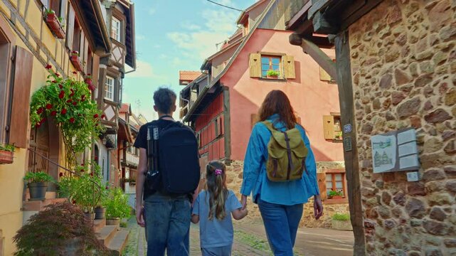 Woman with backpack and children walking on the beautiful street full of colorful houses with flowers of Eguisheim, France 