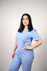 A cheerful, smiling female nurse in a blue medical suit on a white background. Portrait of a young nurse with long dark hair. The image conveys professionalism, compassion, and expertise in healthcare