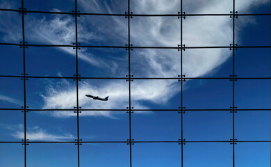 Silhouette of an airplane against a window with square grids and a blue sky and white clouds in the...