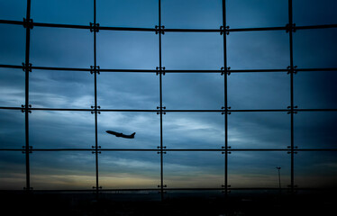 Silhouette of an airplane against a window with square grids and a stormy sky in the background
