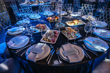 Luxurious round table set with elegant dinnerware, crystal glasses, and an assortment of...
