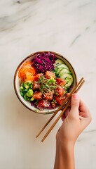 Close-up of colorful poke bowl on marble table hand holding chopsticks