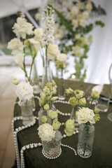 Elegant table setting featuring tall white roses and delicate flowers in glass vases, intertwined with pearl strands on a dark cloth, creating a sophisticated atmosphere.