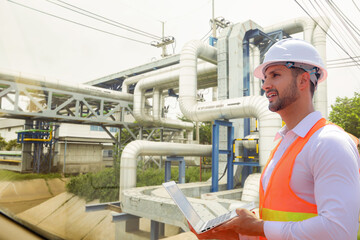 Male architect inspects outside of automotive parts factory inspecting steam pressure pipes covered with stainless steel insulation prevent heat and environmentally friendly nature around the factory.