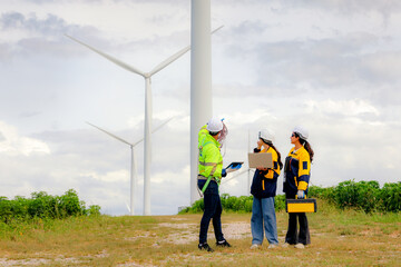 Male and female engineers team walk together wind farm standing tall against cloudy sky sharing...