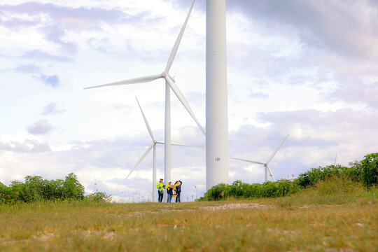 Male and female engineers team walk together wind farm standing tall against cloudy sky sharing ideas about renewable energy from the earth reviewing plans and collecting data on completed mission.