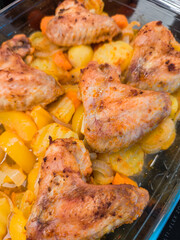 Delicious roasted chicken wings with potatoes, carrots, and onions baking in glass tray