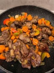 Chicken liver frying in pan with carrots, onions, and peppers